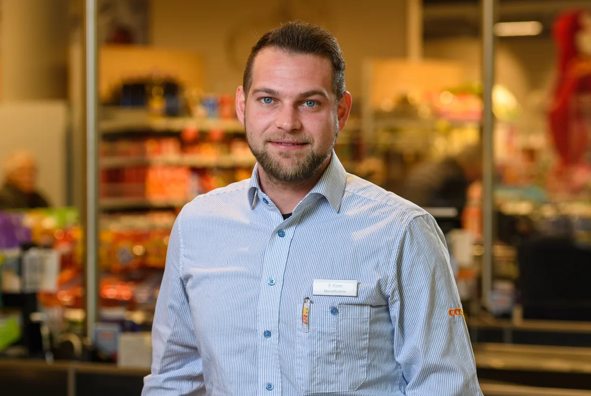 Benjamin Ryser ist neuer Geschäftsführer des Coop-Supermarkts in Pfäffikon. Porträtbild eines Mannes. Er trägt ein blaues Hemd mit Namensschild.